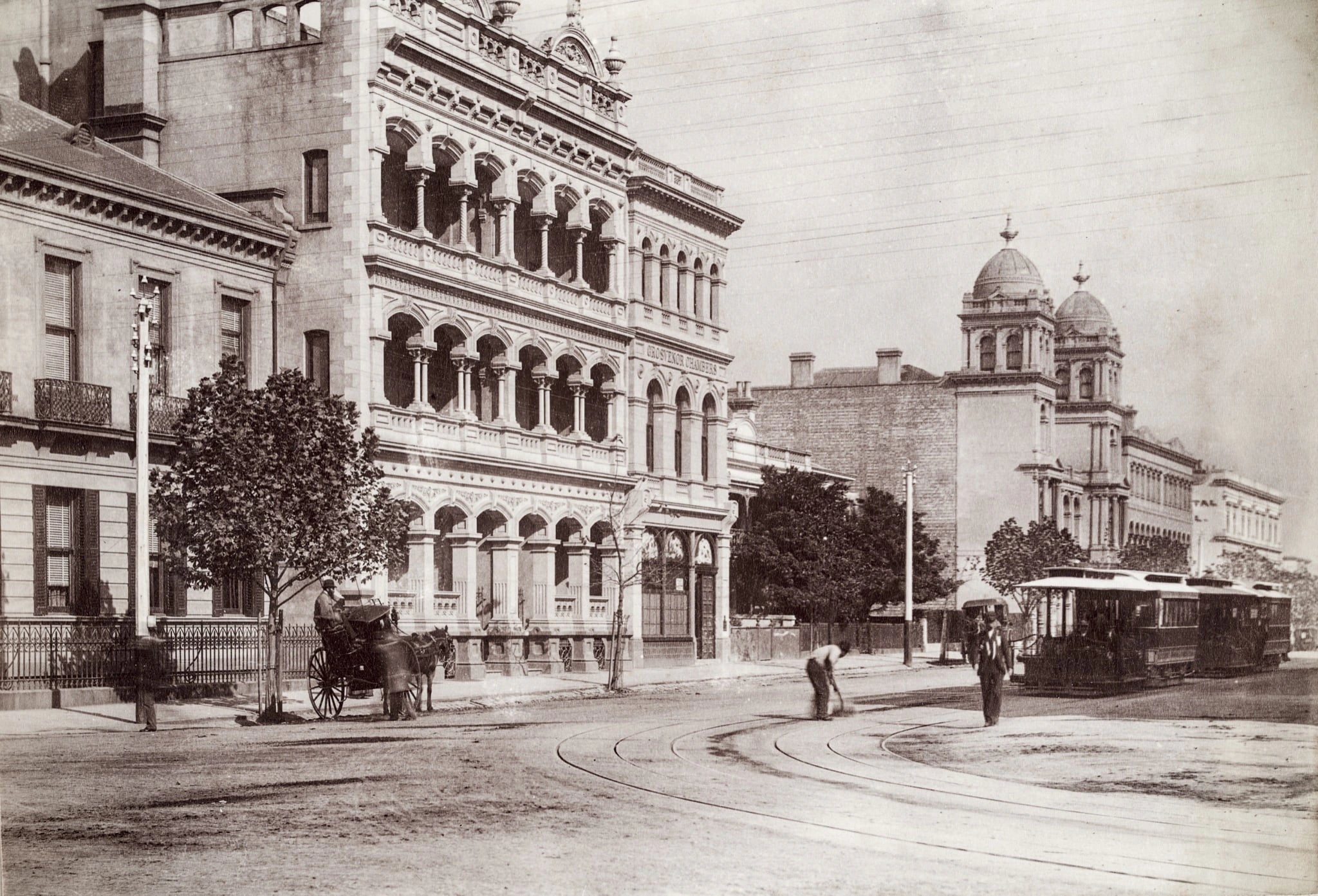 A sepia photograph of Collins Street in the 1880s: the arcaded facade of Grosvenor Chambers on the left, a horse-drawn cab waiting at the kerb, a man sweeping the roadway, and a cable tram and its trailer standing on the rails to the right.